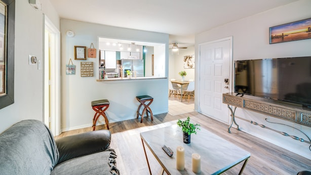 A modern living room with a grey sofa, a coffee table with candles, and a TV on a cabinet. - 9 Mi to Dtwn Dallas: Cozy Couple's Getaway (Dallas)