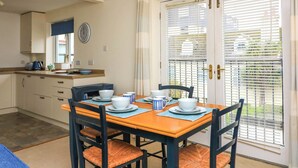 A dining area with a table set for four, chairs with cushioned seats, a kitchen in the background, and a door with blinds. - 8 Dartmouth House (Dartmouth)