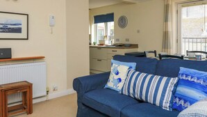 A living room with a blue sofa, a small wooden table, a framed picture on the wall, and a kitchen area in the background. - 8 Dartmouth House (Dartmouth)