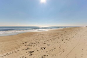Ampia spiaggia sabbiosa con impronte e solchi di pneumatici, che si estende verso l'oceano sotto un cielo sereno.