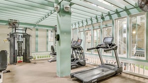 Ett gym med löpband, en styrketräningsmaskin och en fläkt.