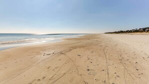 En bred sandstrand med fotspår och däckspår som leder ner till havet.