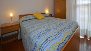A bedroom with a bed, two bedside lamps, a wooden wardrobe, and a window with curtains. - Charming vacation house (Bibione)