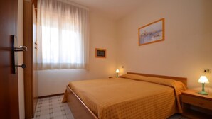Une chambre d’hôtel avec un lit, une table de chevet, une lampe, une fenêtre avec des rideaux et un tableau encadré au mur.