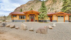 A two-story lodge with a red roof and beige siding, situated in a mountainous area with a gravel driveway and large rocks in front. - On-site River Access: Mtn-view Ouray Oasis! (Ouray)