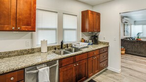 A modern kitchen with granite countertops, stainless steel appliances, wooden cabinets, and a large window with blinds.