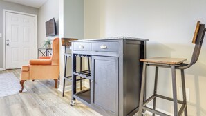 Une pièce avec un plancher en bois, une porte blanche, un meuble gris avec des tiroirs, une petite chaise orange et un tabouret en bois.