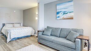 Une chambre à coucher avec un lit, un canapé gris et un tableau représentant une scène de plage.