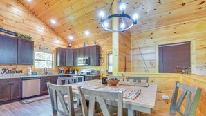 Interior de una cabaña de madera con cocina, comedor y un amplio ventanal.