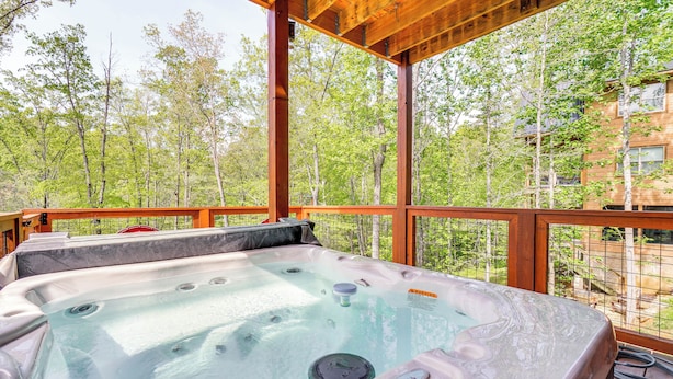 Un jacuzzi en una terraza al aire libre con vistas a un bosque y un edificio al fondo.