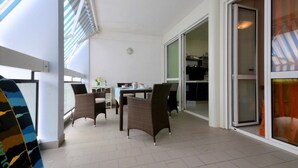 Une pièce comprenant une table à manger et des chaises, une porte-fenêtre coulissante donnant sur un espace cuisine, et offrant une vue sur l’extérieur.