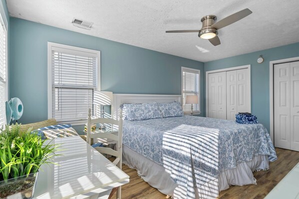 Une chambre à coucher avec un lit, un ventilateur de plafond et une fenêtre avec des stores.