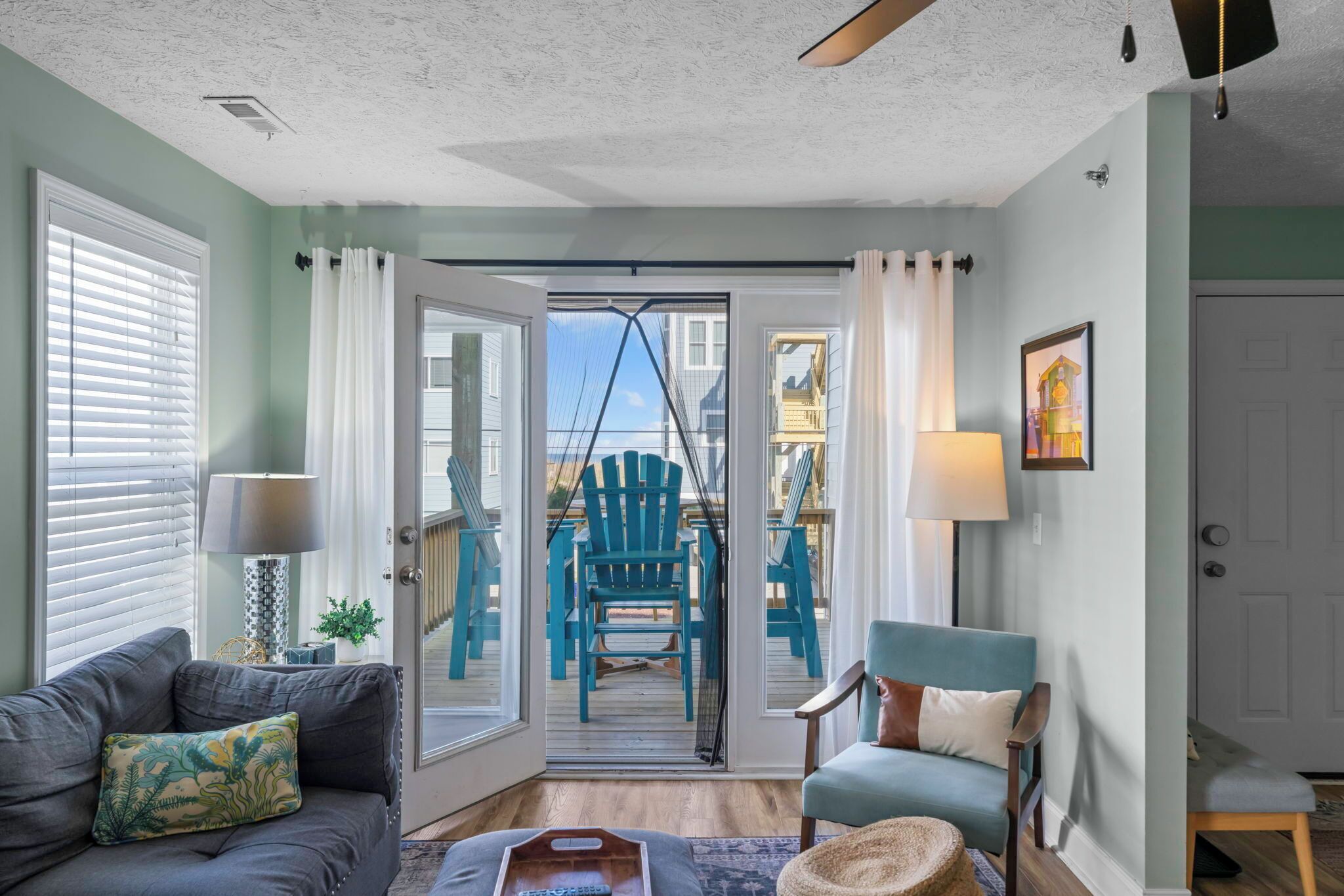 A living room with a sofa, armchair, and a view of a balcony with chairs and a table.