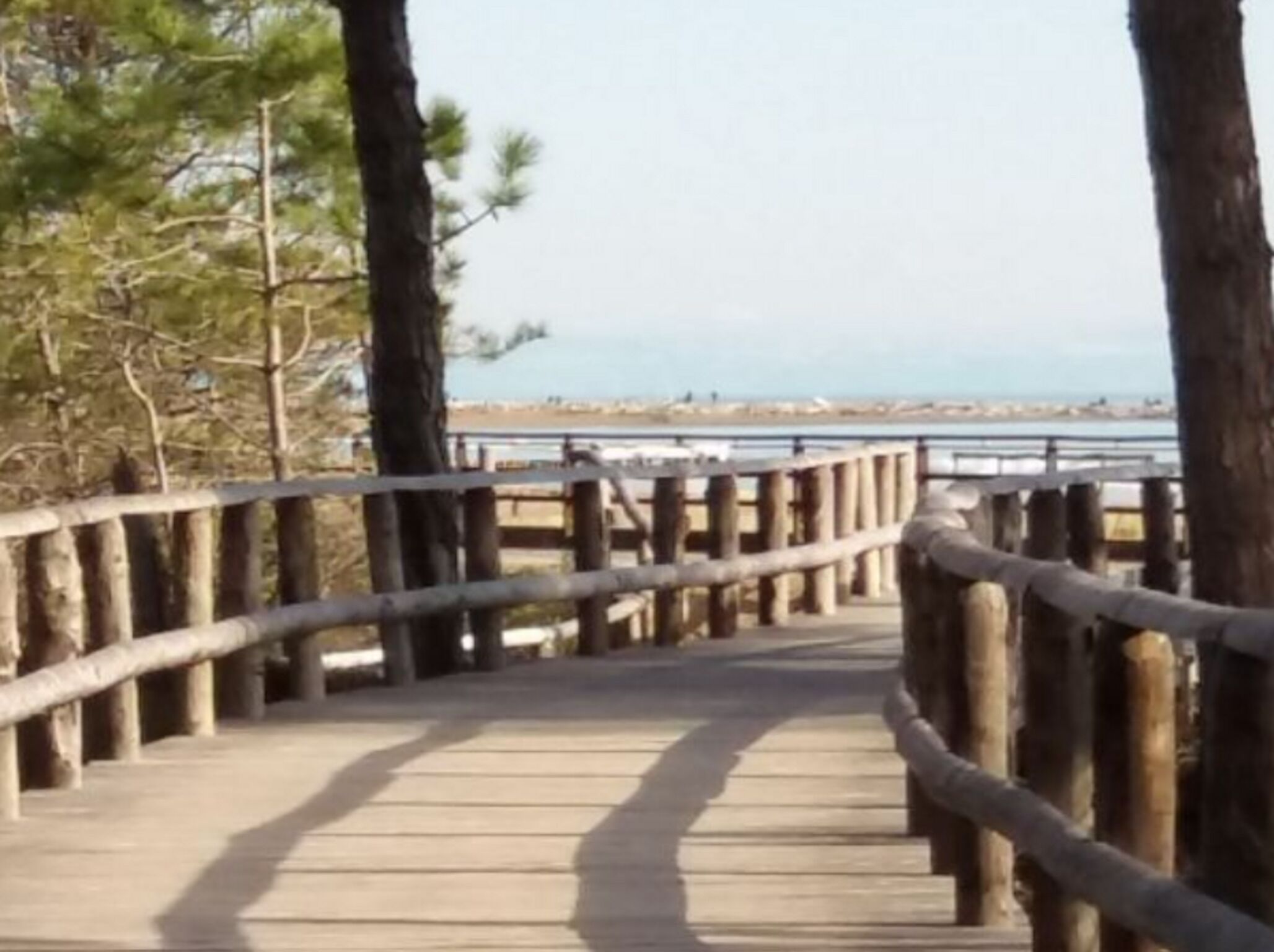 A wooden boardwalk with railings, leading to a beach with a clear view of the ocean and distant shoreline.