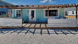 Un edificio costero con terraza de madera, fachada turquesa y cielo despejado.