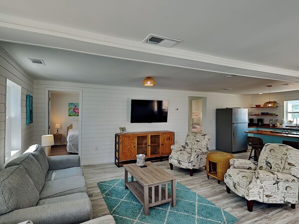 A living room with a gray sofa, a wooden coffee table, patterned armchairs, and a television on the wall. - Salt & Sea A | Fully Renovated, Near Beach (Panama City Beach)