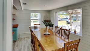 Comedor con una mesa y sillas de madera, una planta en maceta y vistas a la calle a través de ventanas amplias.