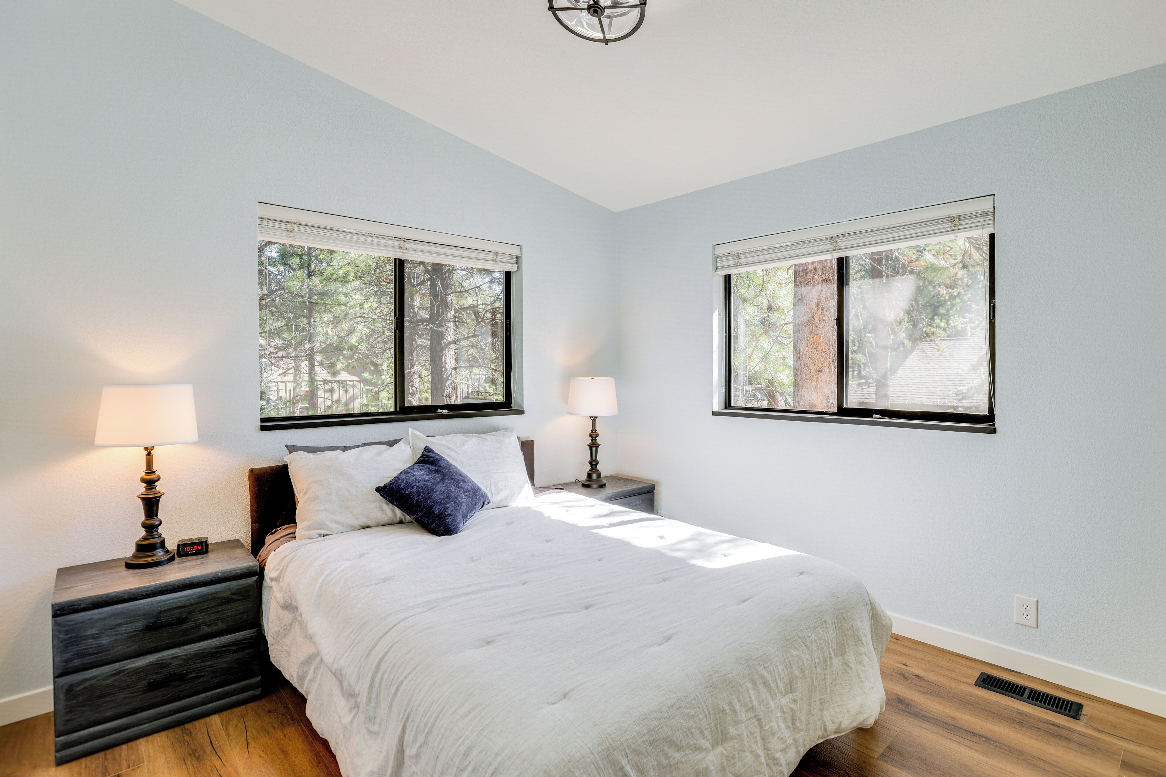 A bedroom with a bed, two bedside tables, two lamps, and two windows.