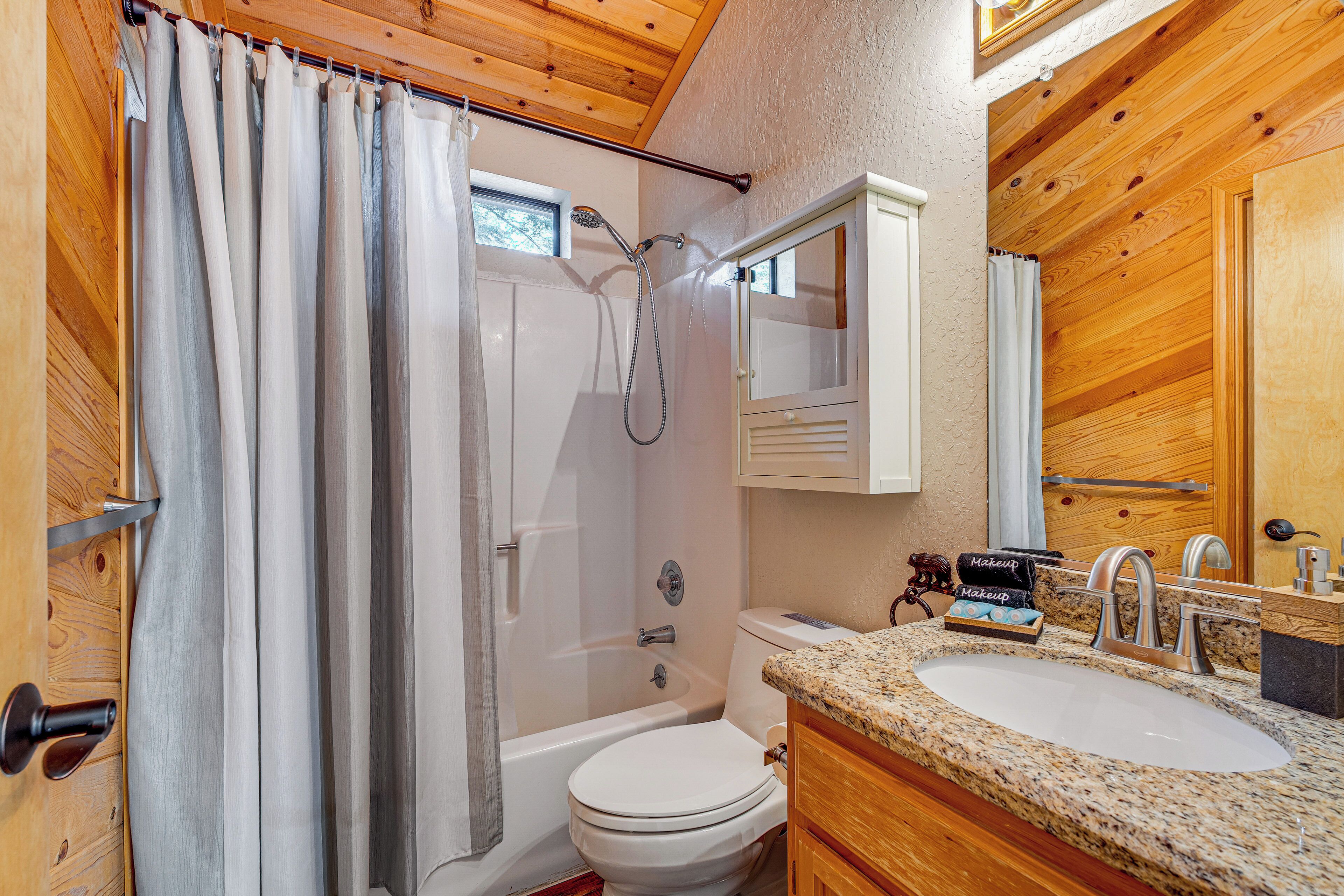 A bathroom with a shower, toilet, sink, and wooden cabinets.