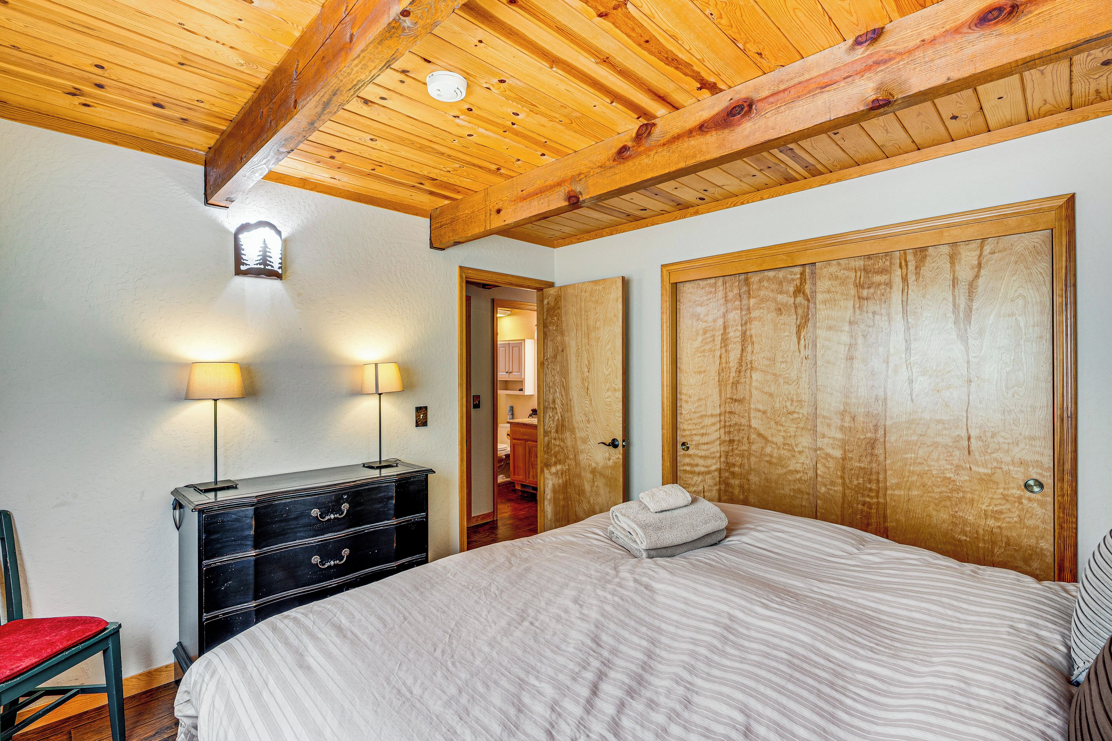 Een slaapkamer met een houten plafond, een bed met een gestreept dekbedovertrek, een dressoir en twee wandlampen.