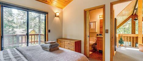 A bedroom with a large bed, a wooden dresser, a nightstand, and a window with a view of trees.
