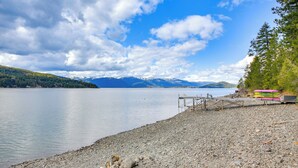 A lakeside view with a rocky shore, a wooden dock, and a row of colorful kayaks. - Peaceful Cabin w/ Dock on Lake Pend Oreille (Sagle)