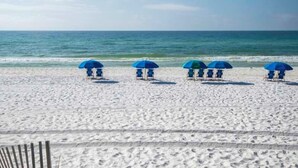 Une plage de sable blanc bordée d’une rangée de parasols de plage bleus.