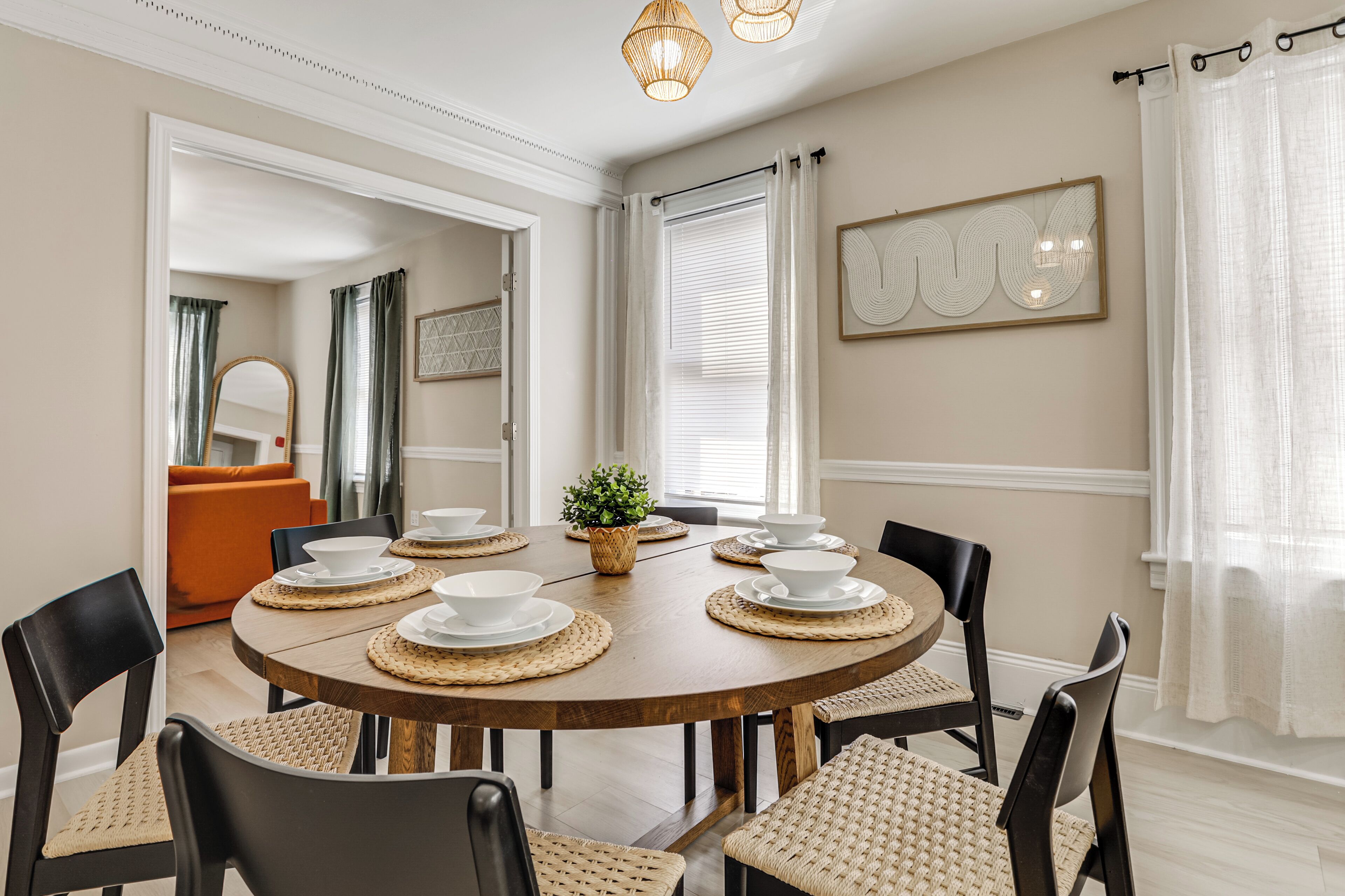 Un coin repas avec une table ronde en bois, dressée pour six personnes, entourée de chaises noires à assise tissée.