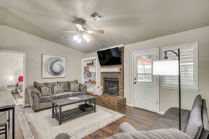 A living room with a sofa, coffee table, fireplace, TV, and a ceiling fan. - 2 Mi to OU: Family-friendly Retreat w/ Patio! (Norman)