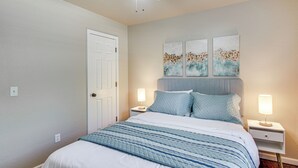Une chambre à coucher comprenant un lit, deux tables de chevet, un ventilateur de plafond et des œuvres d’art accrochées au mur.