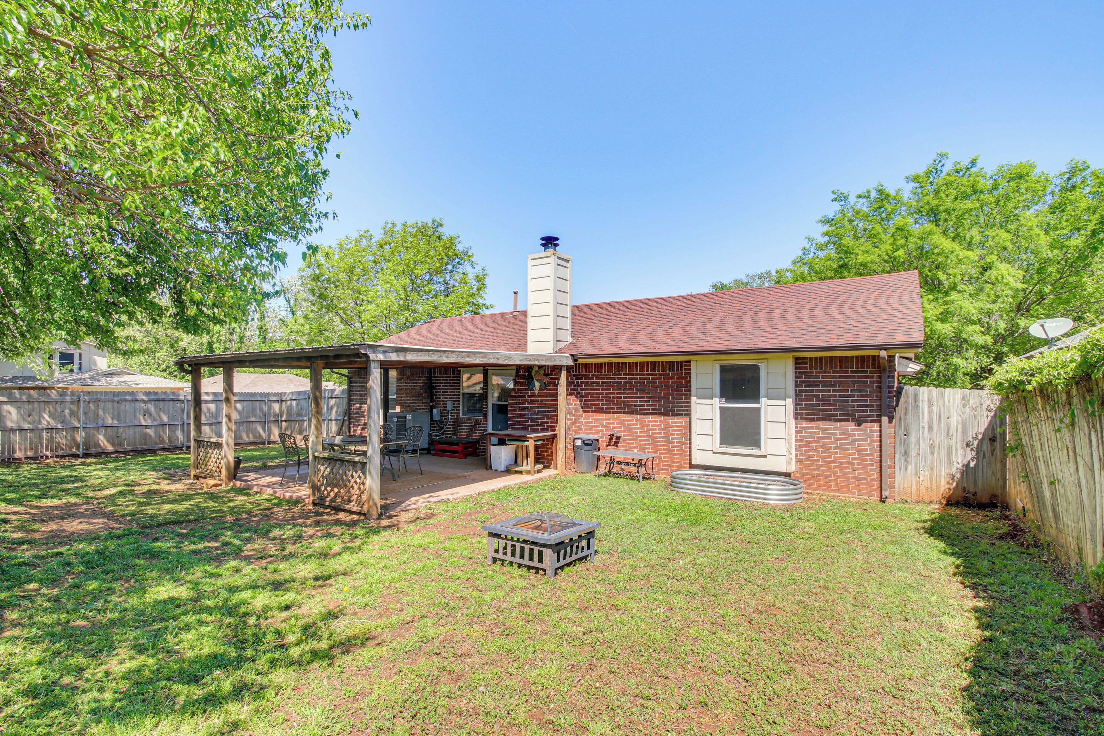 A backyard with a covered patio, a brick house, a chimney, and a fenced area.