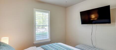 A bedroom with a bed, a window, a ceiling fan, and a TV mounted on the wall.