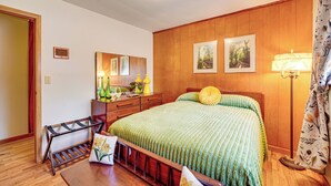 Ein Schlafzimmer mit einem Holz-Kopfteil, einem Bett mit grüner Bettdecke, einem Nachttisch mit Lampe, einem Schminktisch und einem Spiegel an der Wand.