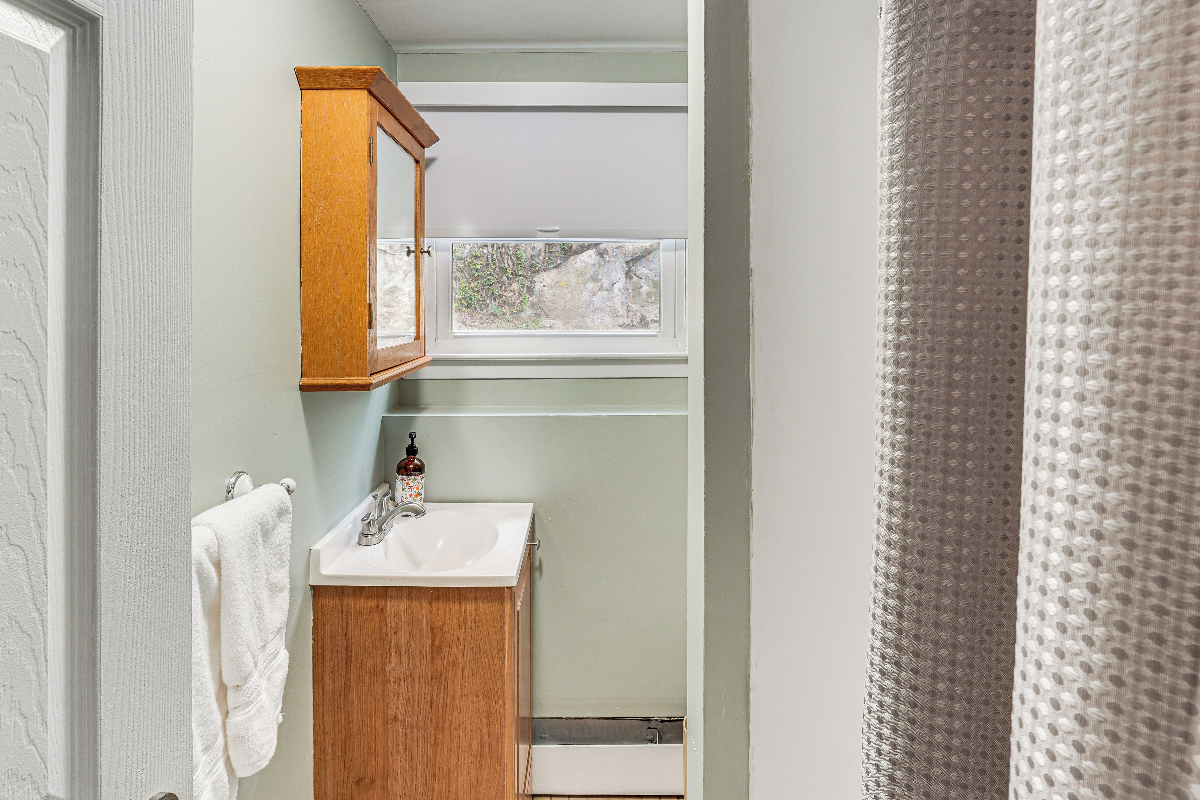 Un baño con un mueble de madera, un lavabo blanco y una ventana sobre el lavabo.