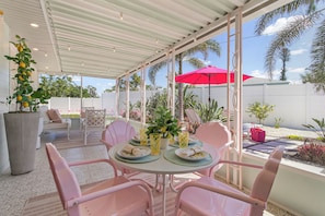 A covered patio with a table set for four, surrounded by pink chairs, and a red umbrella.