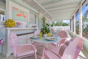 A covered outdoor dining area with pink chairs and a table set for two.