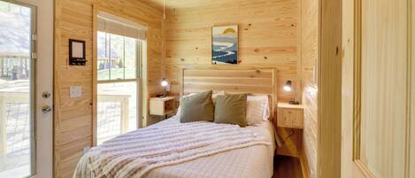 A wooden cabin bedroom with a bed, two bedside tables, a ceiling fan, and a window.