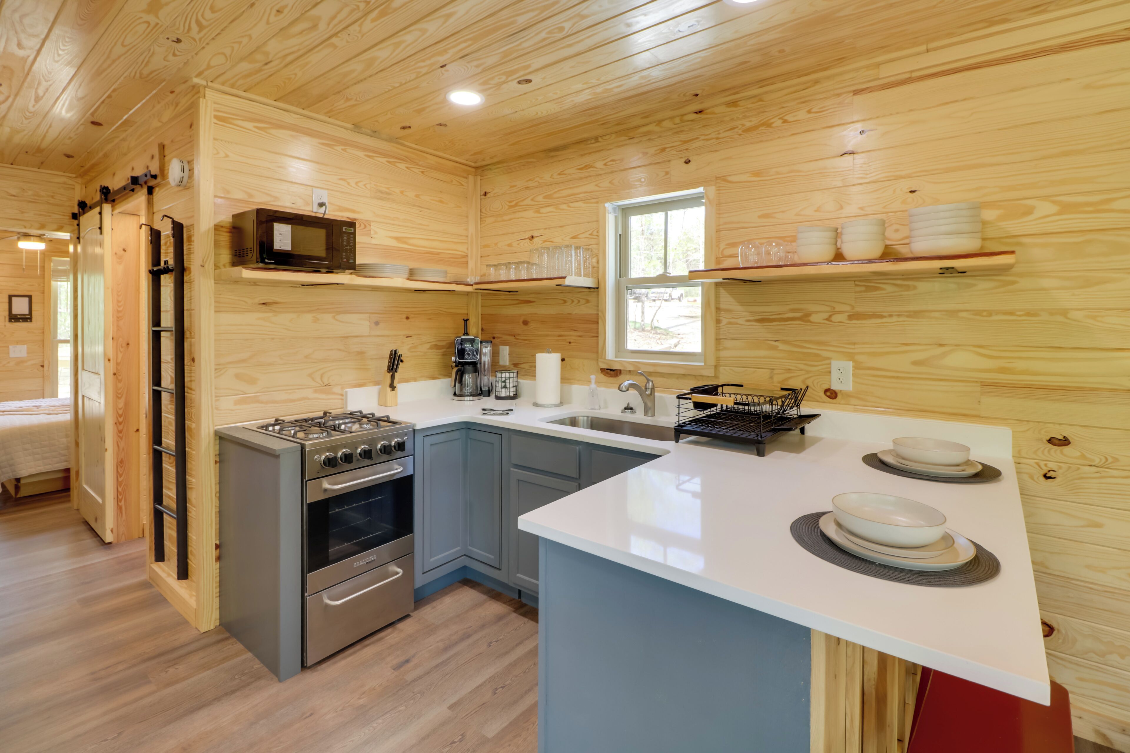 A compact kitchen with a stove, oven, microwave, and sink. There are wooden cabinets and a window providing natural light.