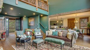 A spacious living area with a high ceiling, wooden staircase, and a view of the kitchen. - Scenic Sanctuary w/ Mtn Views: Glenville Lodge (Glenville)