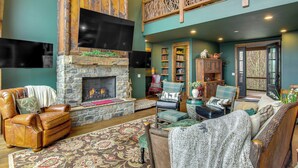A spacious living room with a stone fireplace, leather armchairs, and a high ceiling with a balcony. - Scenic Sanctuary w/ Mtn Views: Glenville Lodge (Glenville)