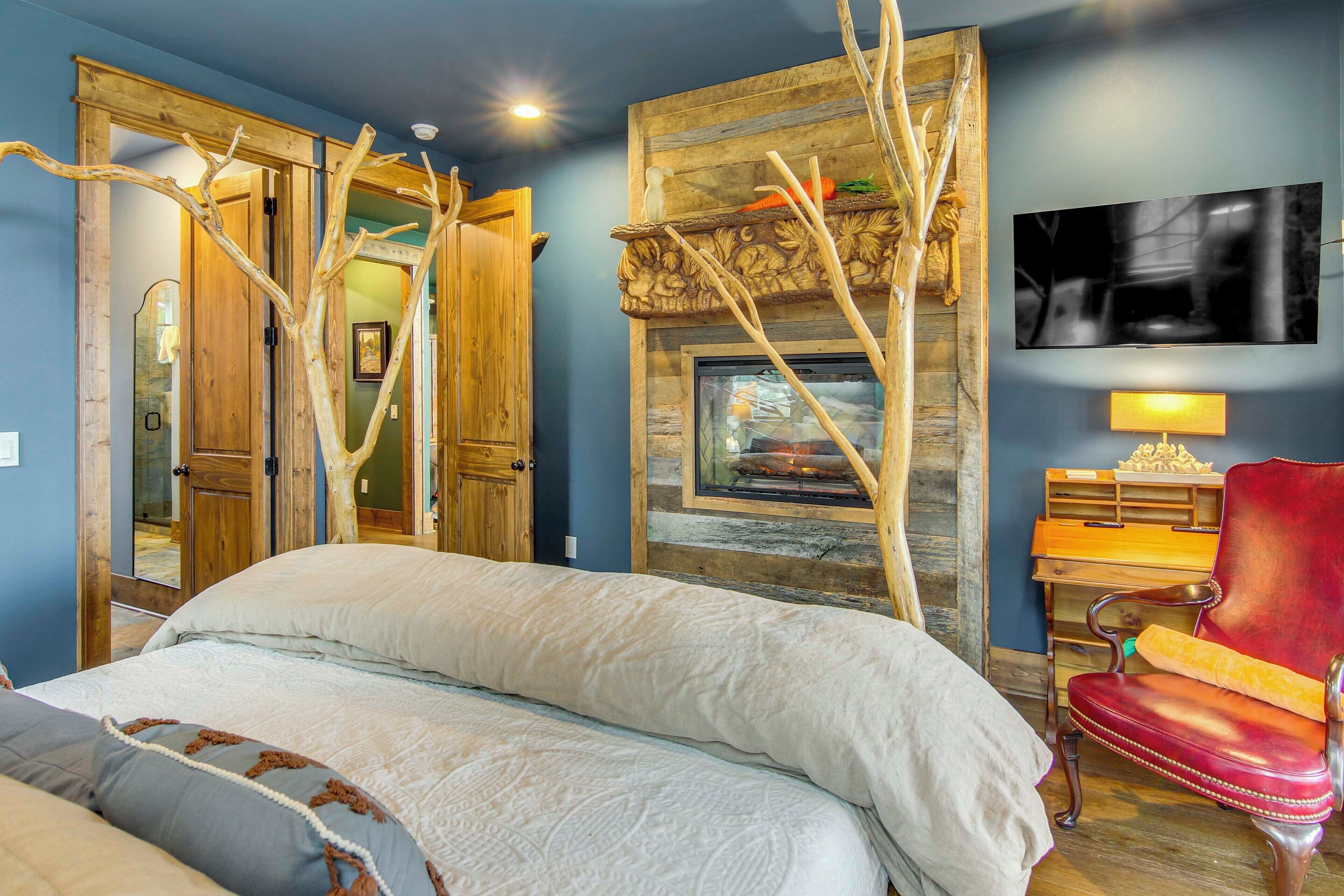A bedroom with a bed, a wooden wardrobe, a fireplace, a red chair, and a television on the wall.