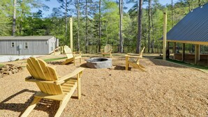 Uma cabana com área de estar externa e lareira, rodeada por uma floresta.