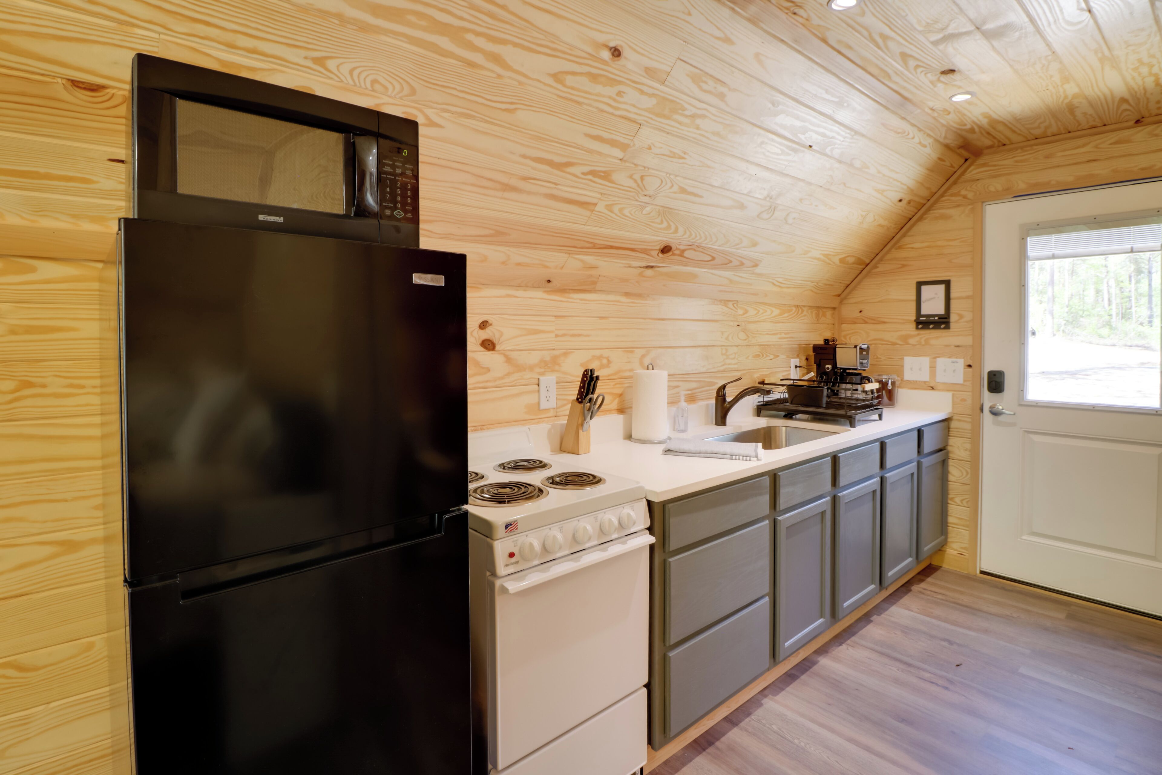 A compact kitchen with a black refrigerator, white stove, and grey cabinets.