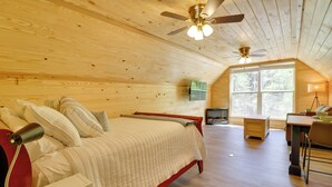 Quarto com cama, mesa de cabeceira, abajur, ventilador de teto e janela grande.