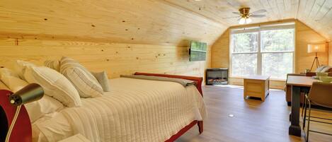 A bedroom with a bed, bedside table, lamp, ceiling fan, and large window.