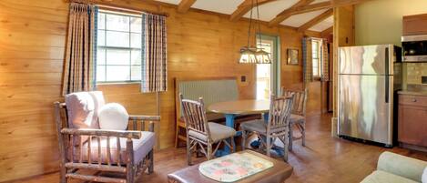 A cozy wooden cabin interior with a dining table, chairs, a sofa, and a refrigerator.