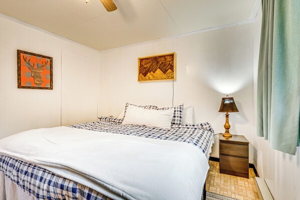 A neatly made bed with a checkered bedspread and pillows, a bedside table with a lamp, and two framed artworks on the wall. - 11 Mi to Massanutten: 'shenandoah River Chalet' (Shenandoah)