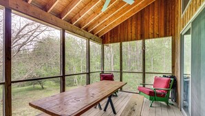 Eine überdachte Veranda mit Holztisch und -stühlen, großen Fenstern und Blick auf den umliegenden Wald.