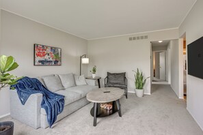 A modern living room with a grey sofa, a round coffee table, a small side table, and a potted plant. - 3 Mi to Dtwn Royal Oak: Getaway w/ Fenced Yard! (Hazel Park)