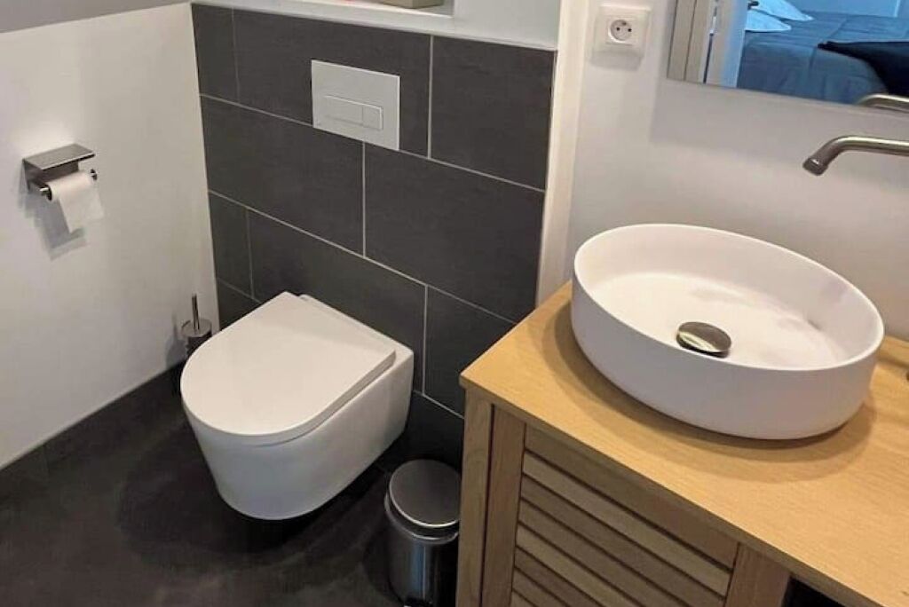 Un baño moderno con inodoro blanco, lavabo redondo y un pequeño cubo de basura.